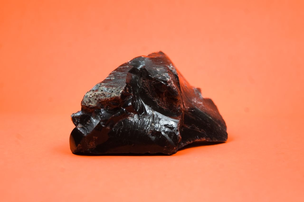 A sharp-focused black obsidian rock displayed on an orange background, showcasing its glossy texture.